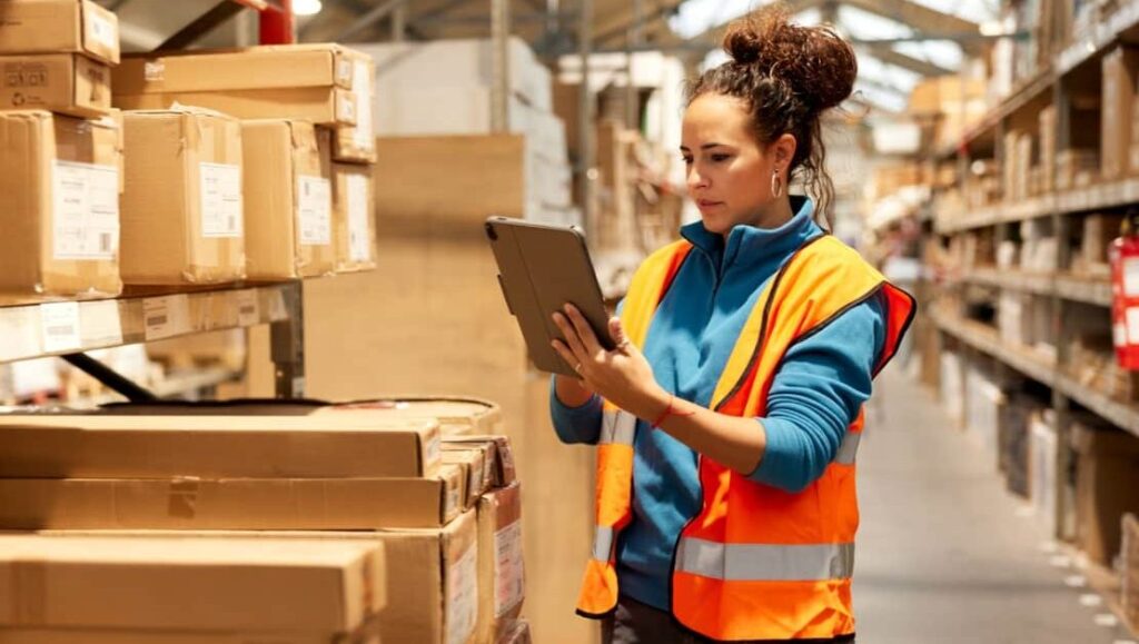 Warehouse worker using a tablet to check inventory on shelves — demonstrates warehouse labor management, workforce optimization, and real-time data visibility for improved productivity and order accuracy.