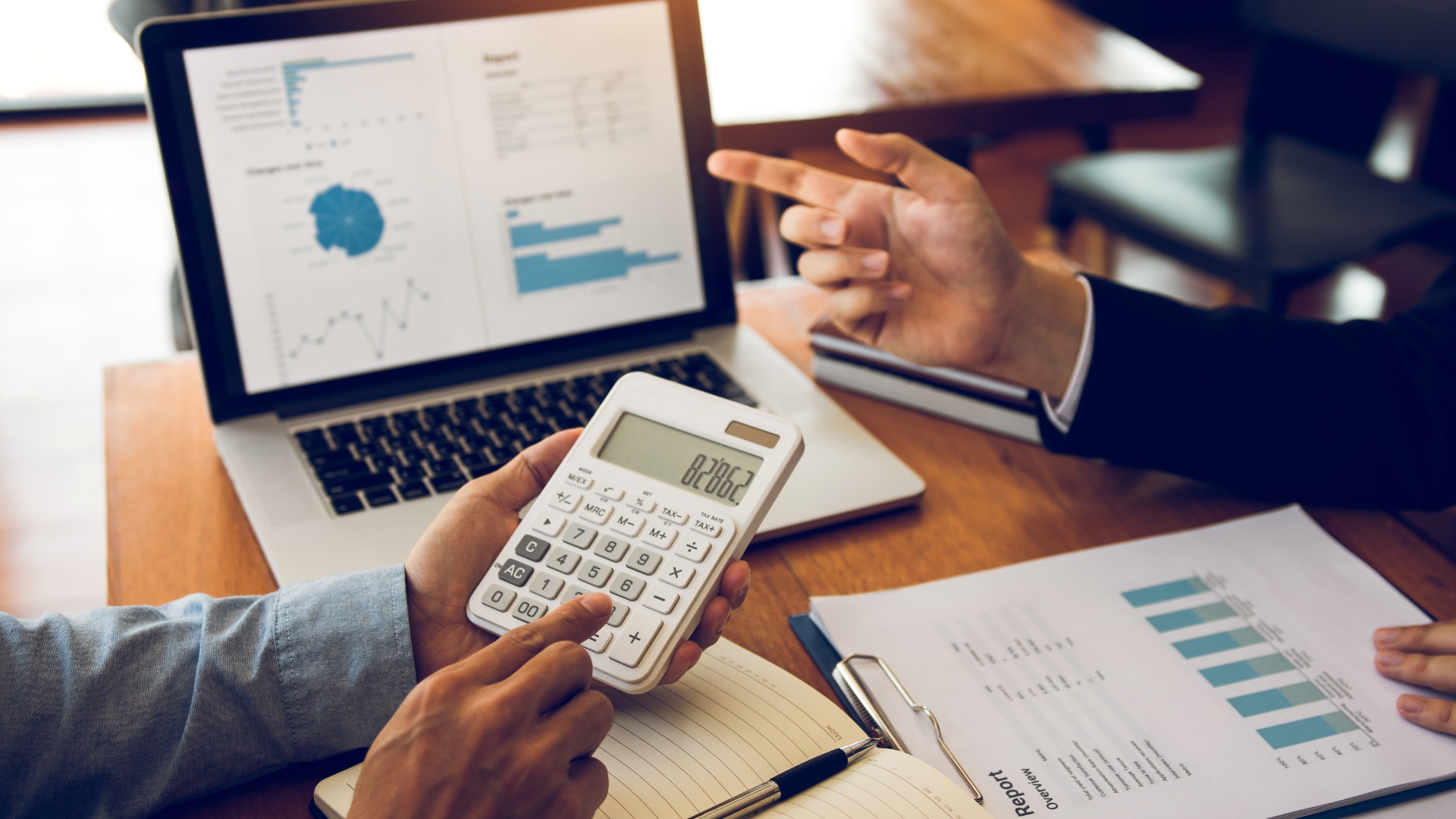 Two people reviewing warehouse cost allocation reports and charts on a laptop, calculating cost-to-serve data for 3PL profitability analysis