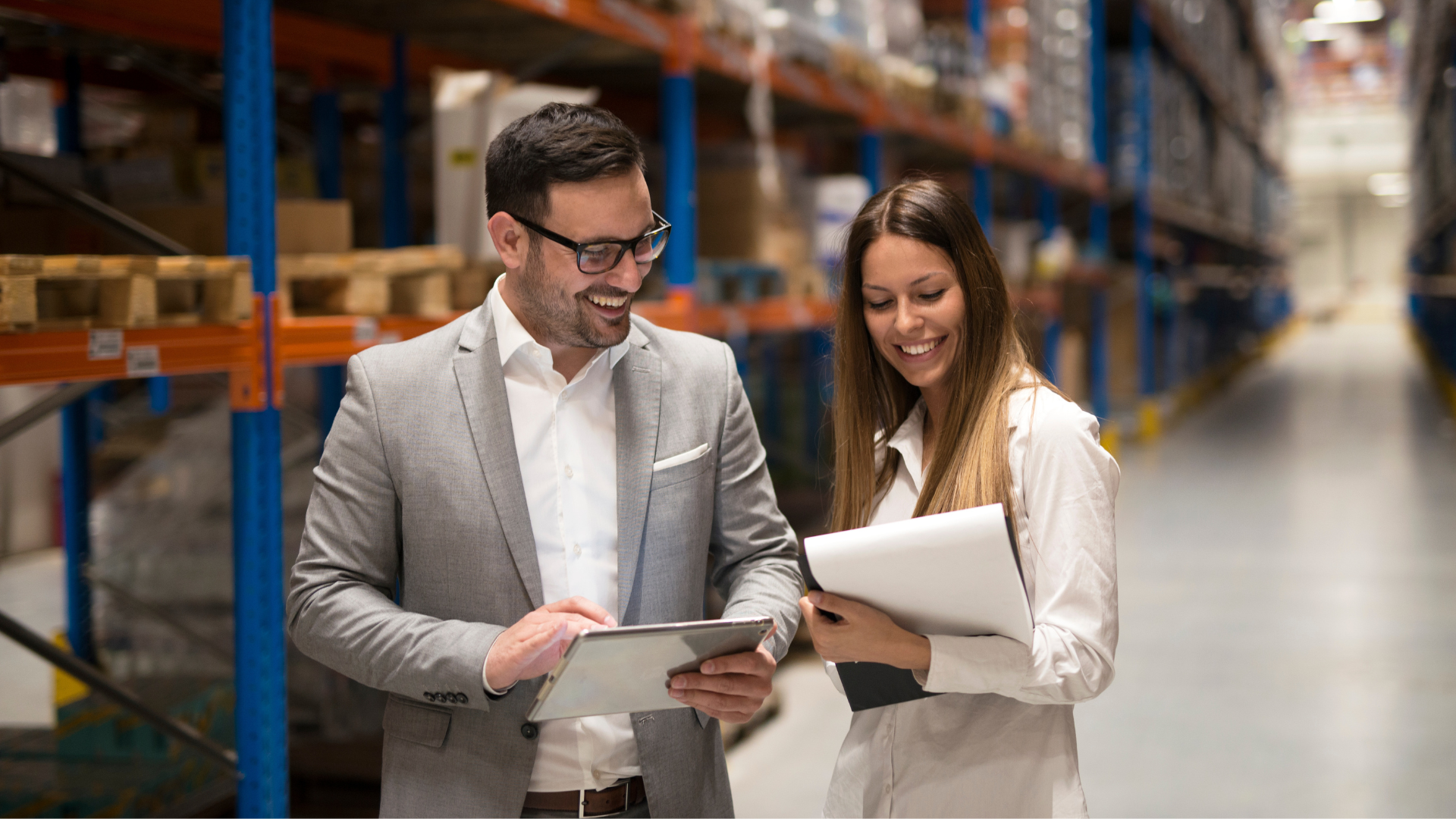 Two warehouse operations managers reviewing multi-site performance data on a tablet while walking through a distribution center