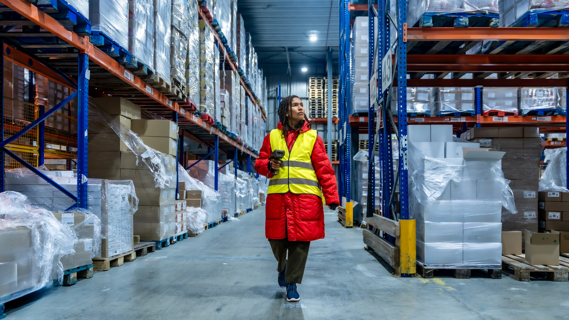 Warehouse associate in cold-weather gear walking a freezer aisle with an RF scanner during a shift