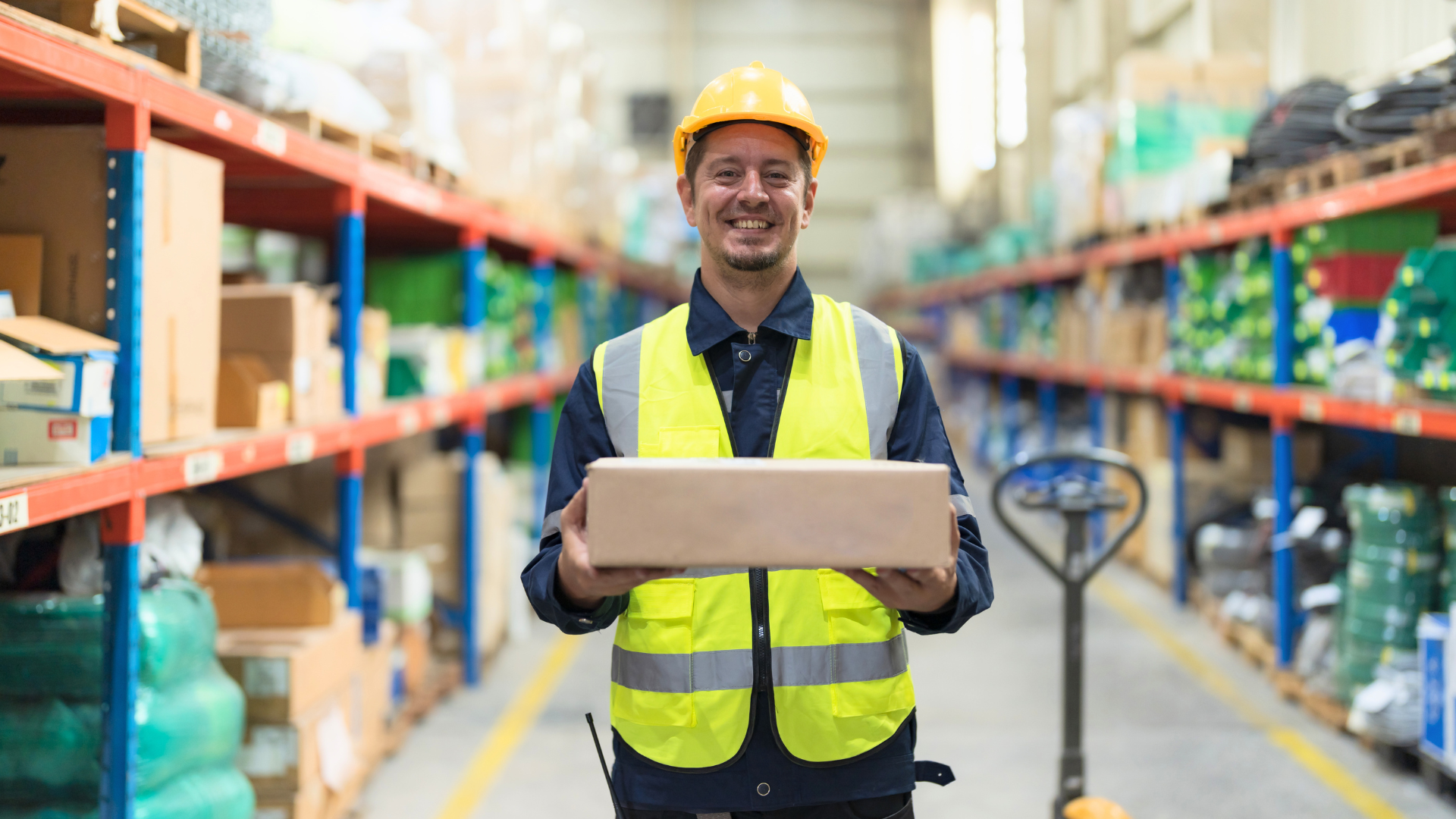 Smiling warehouse worker holding a package near a pallet jack, representing warehouse labor optimization